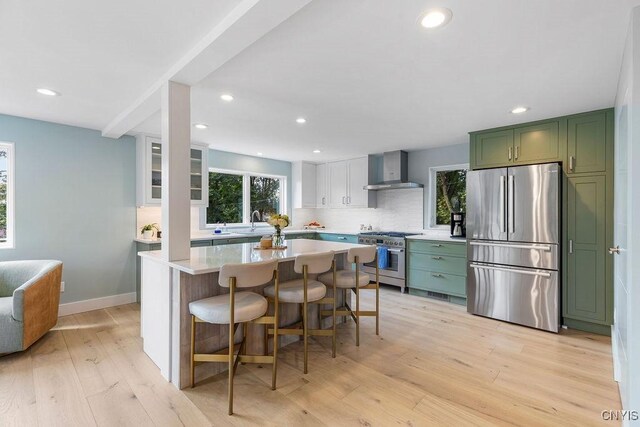 3 Elson Ln, Skaneateles, NY 13152 - kitchen with stainless steel appliances, green cabinetry, wall chimney exhaust hood, decorative backsplash, and light wood-type flooring