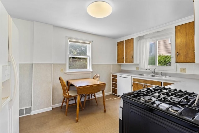 55 Heberton Rd, Irondequoit, NY 14622 - kitchen featuring a sink, white appliances, brown cabinets, healthy amount of natural light, and a wainscoted wall