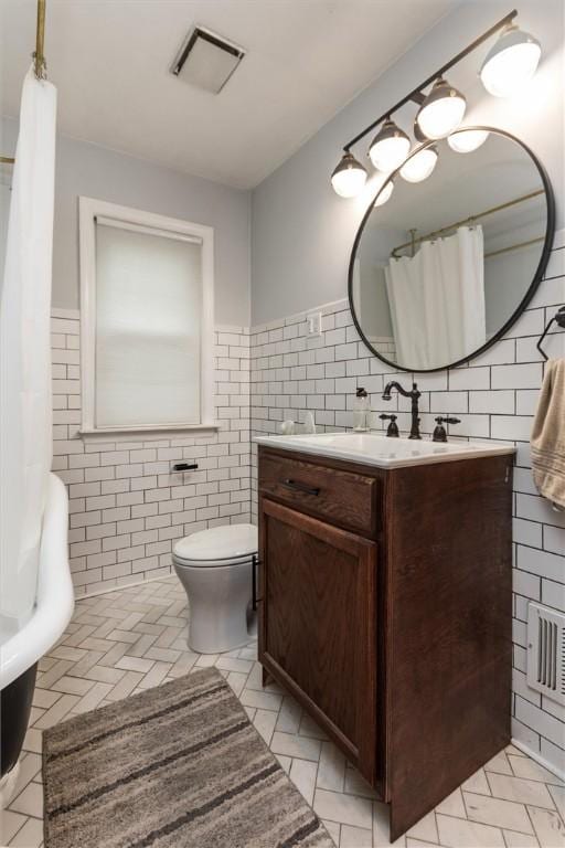 3215 E River Rd, Henrietta, NY 14623 - full bathroom featuring tile walls, toilet, vanity, and a wainscoted wall