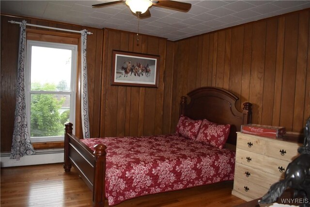 4571 Budd Rd, Cambria, NY 14094 - bedroom with wood finished floors, baseboard heating, wooden walls, and a ceiling fan