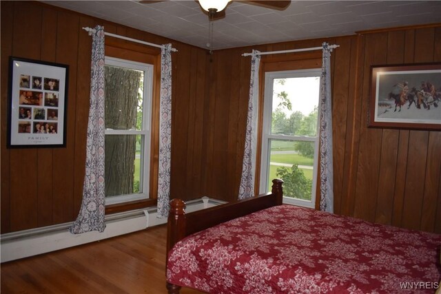 4571 Budd Rd, Cambria, NY 14094 - bedroom featuring baseboard heating, wood finished floors, wooden walls, and a ceiling fan