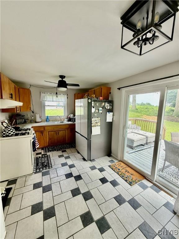 2718 Forest Hill Dr, Fleming, NY 13021 - kitchen featuring freestanding refrigerator, white range with gas stovetop, under cabinet range hood, brown cabinetry, and light countertops