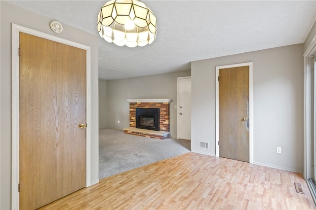 69 Tree Brook Dr, Penfield, NY 14625 - unfurnished living room featuring wood finished floors, a brick fireplace, a textured ceiling, baseboards, and a chandelier