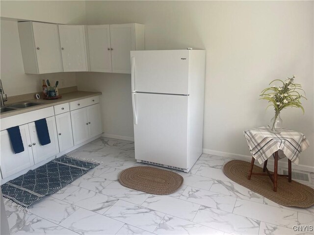 8807 N Main St, Le Ray, NY 13637 - kitchen featuring freestanding refrigerator, light marble finish flooring, a sink, and white cabinetry