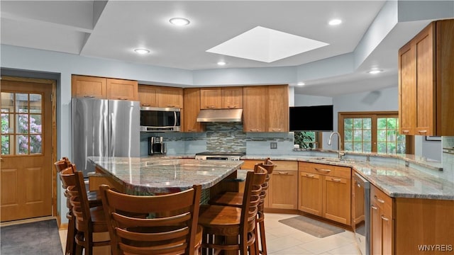 43 Larned Ln, Orchard Park, NY 14127 - kitchen with appliances with stainless steel finishes, under cabinet range hood, a skylight, tasteful backsplash, and a breakfast bar area