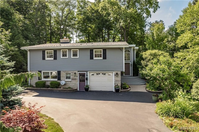43 Larned Ln, Orchard Park, NY 14127 - view of front of house featuring driveway, an attached garage, a chimney, stone siding, and view of scattered trees