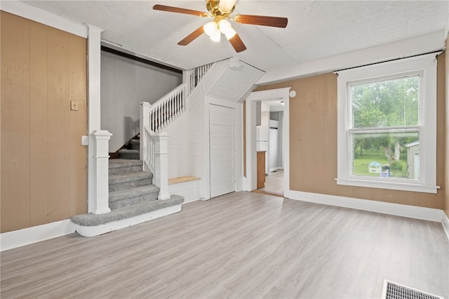 328 W Main St, Palmyra, NY 14522 - unfurnished living room featuring ceiling fan, wood finished floors, stairs, and wooden walls