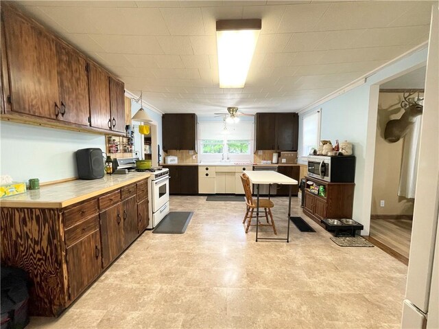 1663 Bingham Rd, Keating Town, PA 16726 - kitchen featuring white gas range, stainless steel microwave, crown molding, light countertops, and a ceiling fan