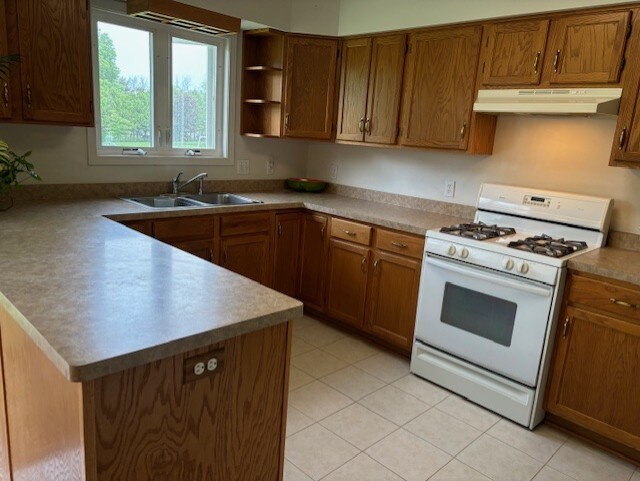 783 Whistlers Cove Ln, Greece, NY 14612 - kitchen featuring white gas stove, under cabinet range hood, a peninsula, brown cabinetry, and open shelves