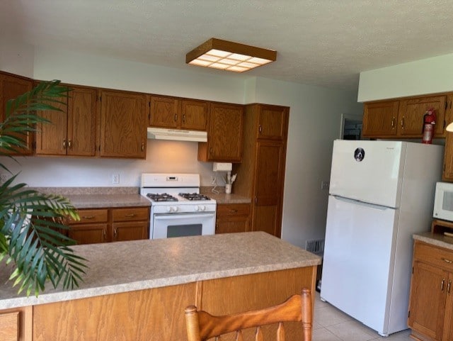 783 Whistlers Cove Ln, Greece, NY 14612 - kitchen featuring white appliances, brown cabinets, under cabinet range hood, light countertops, and light tile patterned flooring