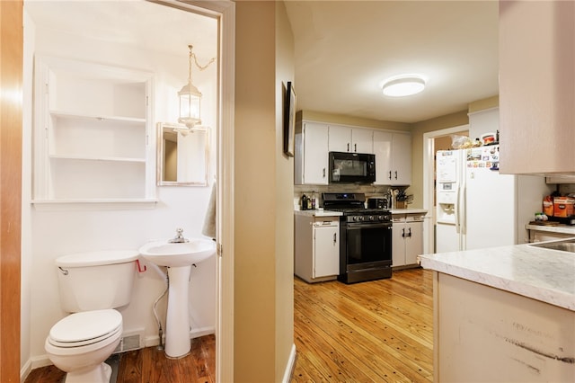 3389 Culver Rd, Irondequoit, NY 14622 - kitchen with black microwave, gas range, light wood-style floors, white cabinetry, and white fridge with ice dispenser