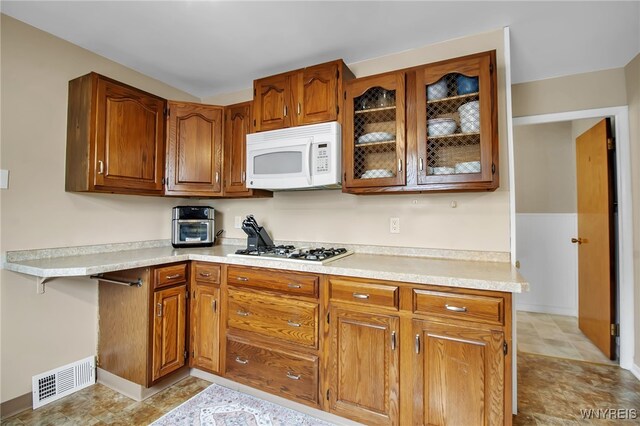774 Loretta St, Tonawanda-Town, NY 14150 - kitchen with white microwave, gas stovetop, brown cabinetry, light countertops, and glass insert cabinets