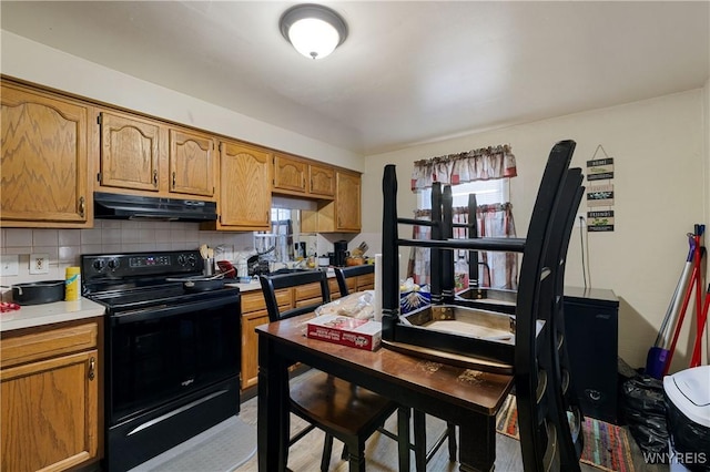 2320 Niagara St, Niagara Falls, NY 14303 - kitchen with black / electric stove, under cabinet range hood, light countertops, decorative backsplash, and brown cabinetry
