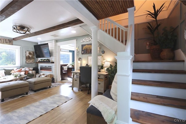 31768 Wilton Rd, Rutland, NY 13619 - living room featuring beamed ceiling, wood finished floors, a large fireplace, stairs, and decorative columns