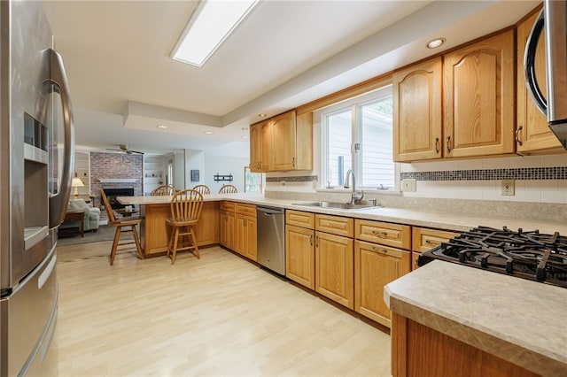 208 Blackwell Ln, Henrietta, NY 14467 - kitchen with appliances with stainless steel finishes, a peninsula, light countertops, a brick fireplace, and light wood-style flooring