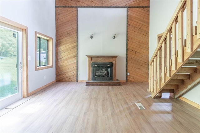 46946 Dingman Point Rd, Alexandria, NY 13607 - unfurnished living room with stairway, wood finished floors, wooden walls, a towering ceiling, and a fireplace with raised hearth