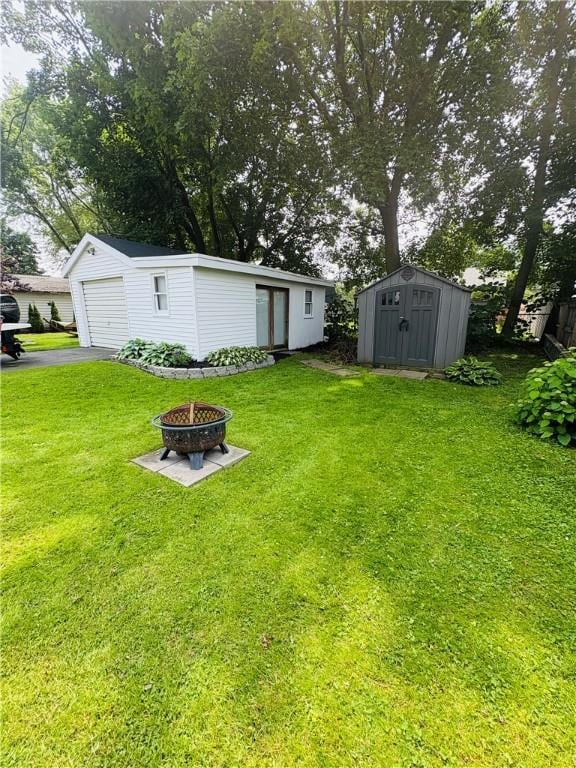 216 W William St Unit 201, Corning-City, NY 14830 - view of grassy yard featuring an outdoor fire pit, a garage, a storage unit, and driveway