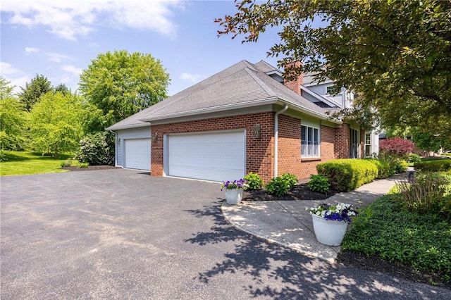 15 Cathedral Oaks, Perinton, NY 14450 - view of property exterior with driveway, brick siding, a garage, roof with shingles, and a chimney