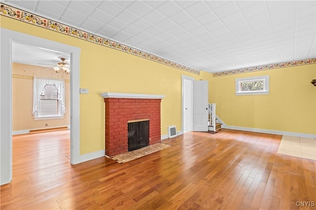 500 Glenwood Ave, Syracuse, NY 13207 - unfurnished living room with hardwood / wood-style flooring, a brick fireplace, ceiling fan, and stairway