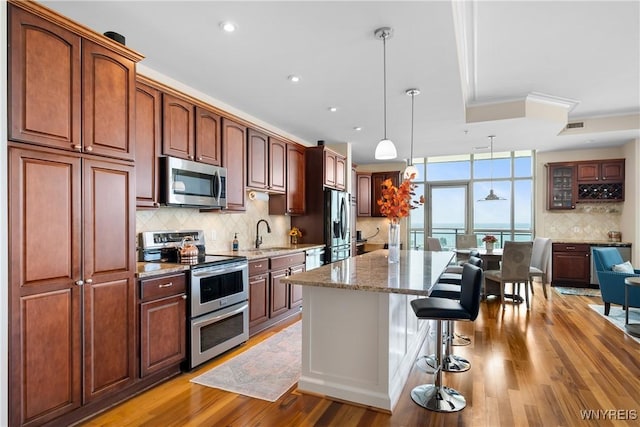 132 Lakefront Blvd Unit 804, Buffalo, NY 14202 - kitchen featuring appliances with stainless steel finishes, tasteful backsplash, a breakfast bar area, light wood-type flooring, and a center island