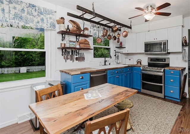 5458 Oxbow Rd, Cazenovia, NY 13035 - kitchen with blue cabinets, stainless steel appliances, wooden counters, open shelves, and light wood-style floors