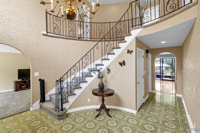 212 Crestwood Ln, Amherst, NY 14221 - stairs featuring arched walkways, a textured wall, a chandelier, and a towering ceiling