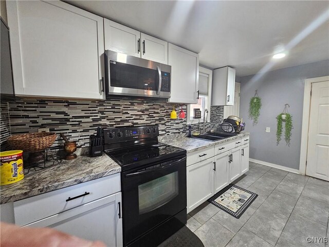 6 Bryant St, Utica, NY 13502 - kitchen with stainless steel microwave, black electric range, backsplash, white cabinetry, and light tile patterned floors
