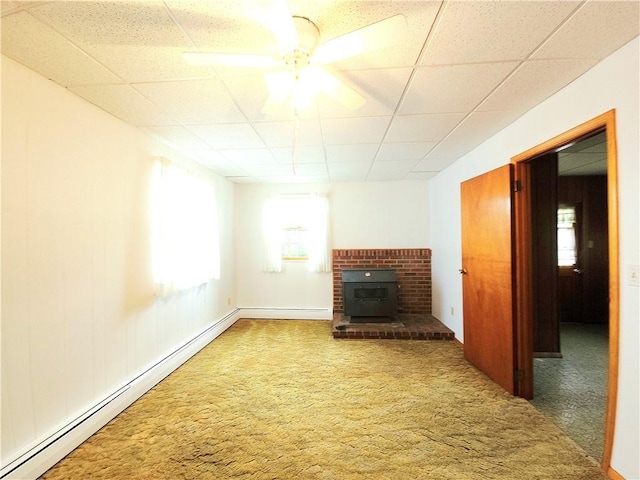 4883 Pinecrest Rd, Veteran, NY 14864 - unfurnished living room featuring a baseboard radiator, a paneled ceiling, a wood stove, carpet floors, and ceiling fan