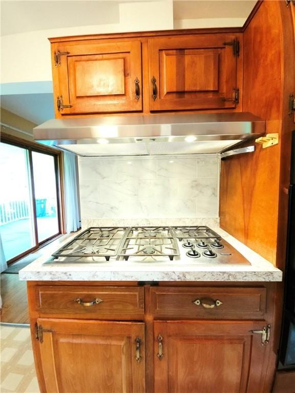 4883 Pinecrest Rd, Veteran, NY 14864 - kitchen with under cabinet range hood, stainless steel gas cooktop, brown cabinets, and decorative backsplash