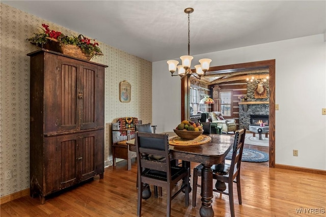 8345 Lapp Rd, Clarence, NY 14051 - dining room with light wood-style floors, a chandelier, a stone fireplace, and wallpapered walls
