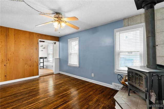 55 Spruce Rd, Amherst, NY 14226 - unfurnished room featuring a wood stove, wood finished floors, a ceiling fan, a textured ceiling, and wooden walls