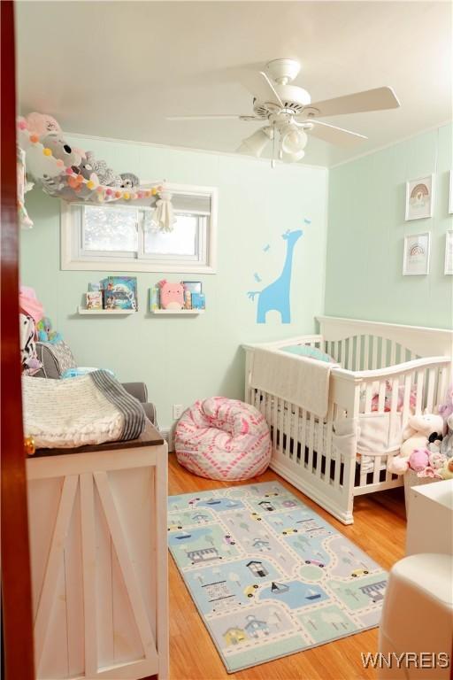 1422 Master St, North Tonawanda, NY 14120 - bedroom featuring a nursery area, wood finished floors, and a ceiling fan