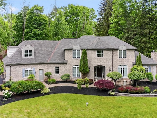 1010 Plank Rd, Penfield, NY 14580 - french country style house featuring a front lawn, a shingled roof, stone siding, and a chimney