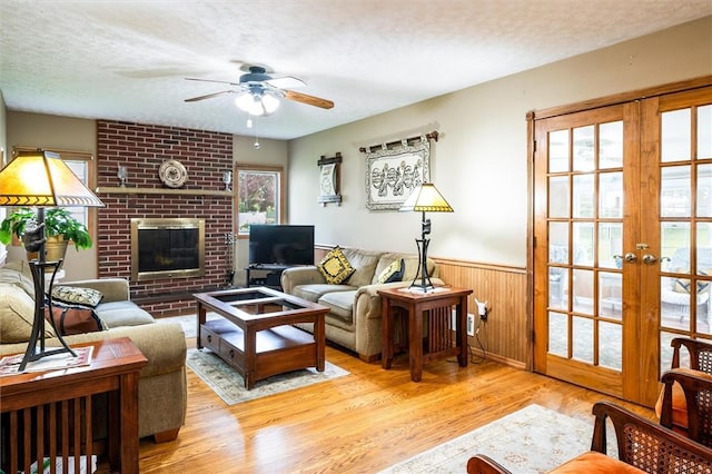 217 Red Lion Rd, Henrietta, NY 14467 - living area with wood finished floors, ceiling fan, a brick fireplace, a wainscoted wall, and french doors