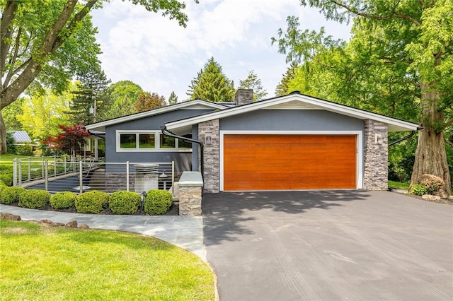 5 Elmwood Hill Ln, Brighton, NY 14610 - view of front of house with stone siding, driveway, an attached garage, a chimney, and stucco siding