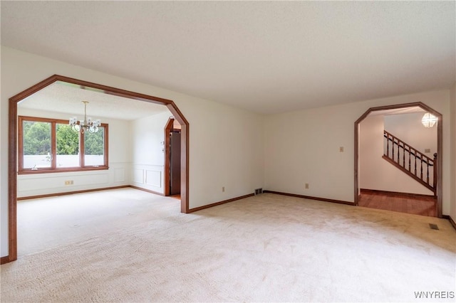64 Bywater Dr, Amherst, NY 14068 - empty room featuring light carpet, arched walkways, a chandelier, stairway, and wainscoting