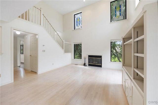 4797 Huntwood, Manlius, NY 13104 - unfurnished living room featuring light wood-style flooring, a glass covered fireplace, a high ceiling, and stairs