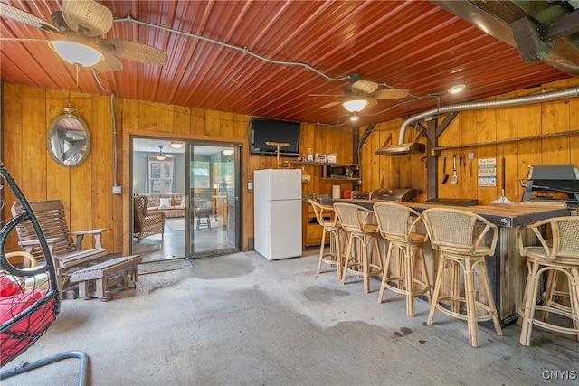 2012 Pleasant Ave, Vienna, NY 13308 - kitchen with freestanding refrigerator, a ceiling fan, wood walls, stainless steel microwave, and concrete floors