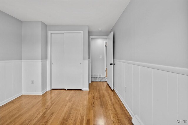 8478 Grandview Dr, Cicero, NY 13039 - unfurnished bedroom with light wood-style floors, a wainscoted wall, and a closet