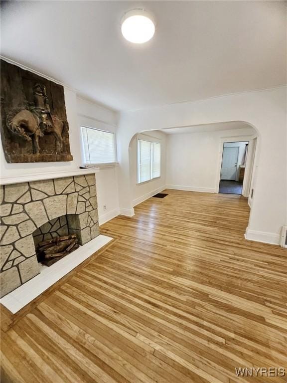 269 Westminster Ave, Buffalo, NY 14215 - unfurnished living room featuring arched walkways, light wood finished floors, and a stone fireplace