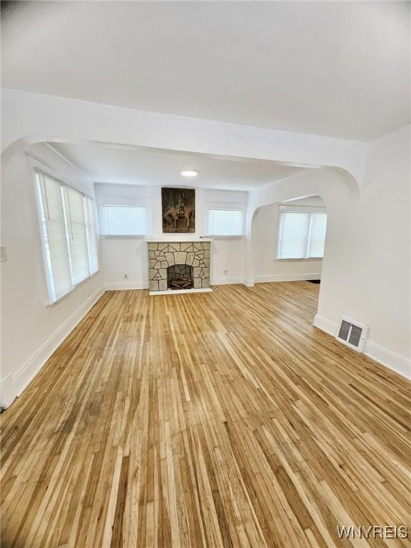 269 Westminster Ave, Buffalo, NY 14215 - unfurnished living room featuring light wood-style flooring, arched walkways, and a fireplace