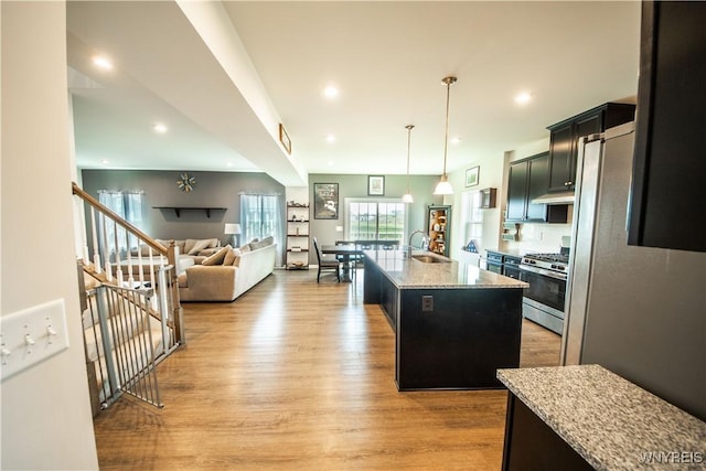 510 Limestone Ct, Grand Island, NY 14072 - kitchen featuring stainless steel gas stove, a center island with sink, dark cabinetry, light stone counters, and light wood-type flooring