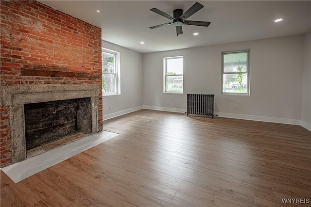 7395 W Somerset Rd, Somerset, NY 14008 - unfurnished living room featuring radiator heating unit, a brick fireplace, wood finished floors, ceiling fan, and recessed lighting