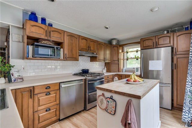 10256 State Route 26, Denmark, NY 13367 - kitchen with stainless steel appliances, under cabinet range hood, light wood finished floors, decorative backsplash, and a textured ceiling