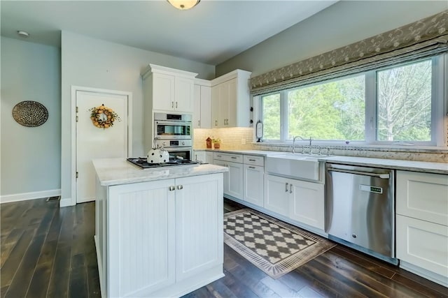 1544 Paddy Ln, Macedon, NY 14502 - kitchen featuring appliances with stainless steel finishes, dark wood finished floors, white cabinets, backsplash, and a kitchen island
