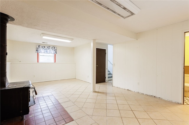 12 Rawhide Dr, Henrietta, NY 14586 - basement featuring a wood stove, light tile patterned floors, stairway, and a decorative wall