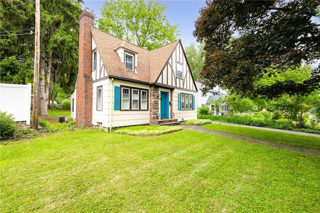 25 Kiniry Dr, Irondequoit, NY 14609 - tudor house featuring a chimney, a front lawn, roof with shingles, and board and batten siding
