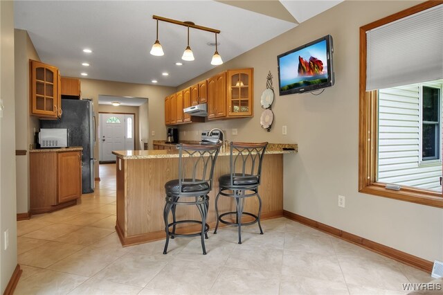 139 Autumn Creek Ct, Amherst, NY 14051 - kitchen featuring under cabinet range hood, a peninsula, glass insert cabinets, brown cabinetry, and recessed lighting