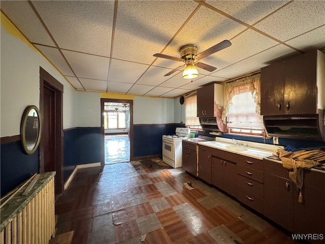 64 Timon St, Buffalo, NY 14211 - kitchen featuring white gas range, a drop ceiling, ceiling fan, wainscoting, and dark wood-style floors