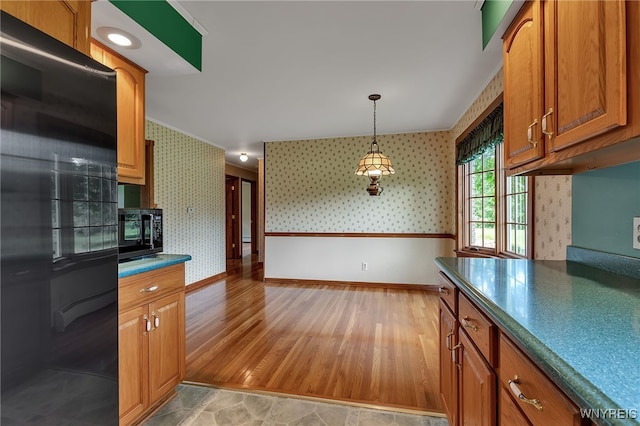218 Hall Rd, Lancaster, NY 14059 - kitchen with wallpapered walls, black appliances, brown cabinetry, dark countertops, and pendant lighting